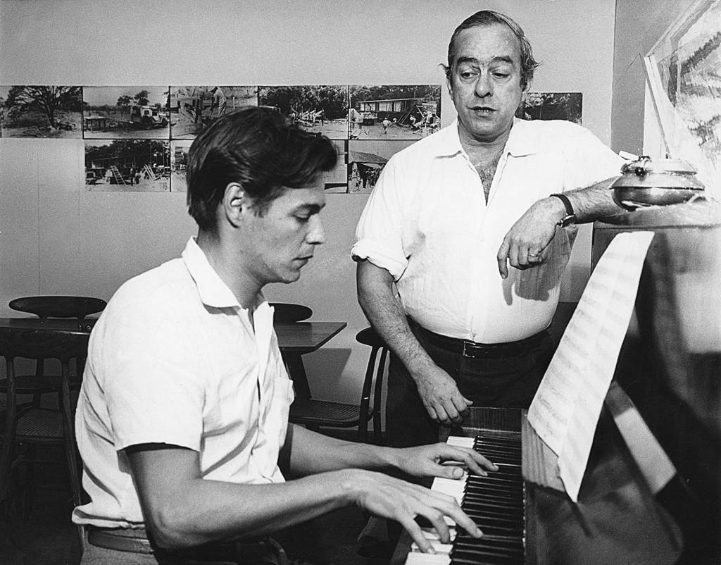 Tom Jobim sentado ao piano e Vinicius de Moraes ao lado dele, com o braço apoiado no instrumento