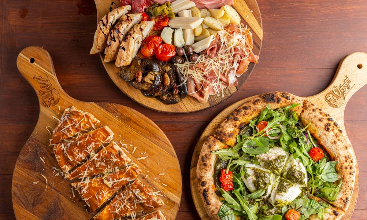 A imagem mostra três tábuas com pizza, frios e massa de pão