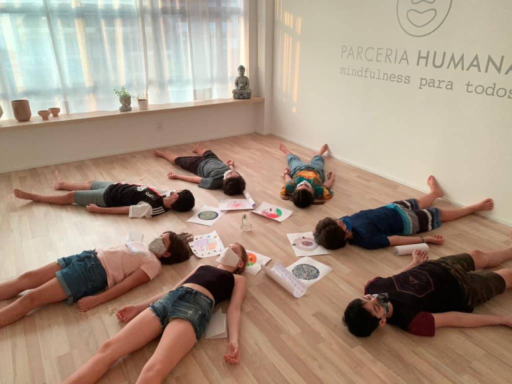 Crianças deitadas no chão, em círculo, com papéis desenhados também no chão