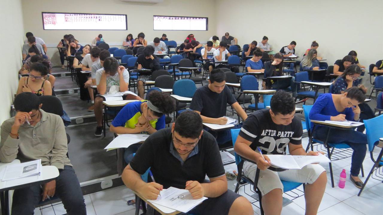 A imagem mostra uma sala de aula onde jovens fazem a prova do Exame Nacional do Ensino Médio (Enem)