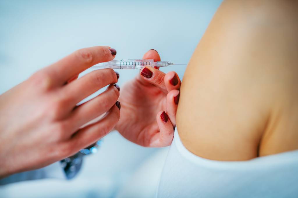 Mulher aplica a vacina no braço de uma pessoa.