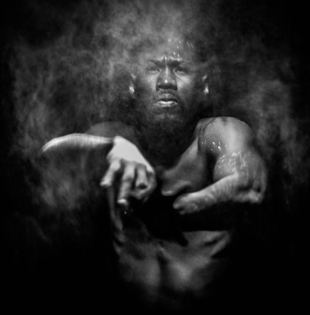 Fotografia em preto e branco de homem com fumaça próxima a seu rosto
