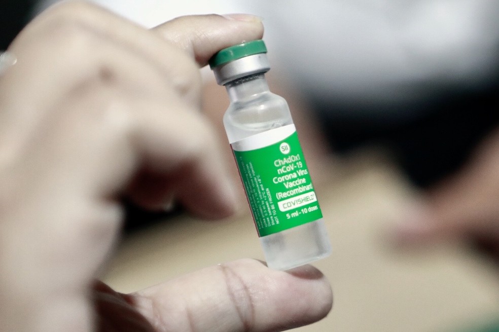 A imagem mostra uma mão de luva segurando uma ampola de vacina