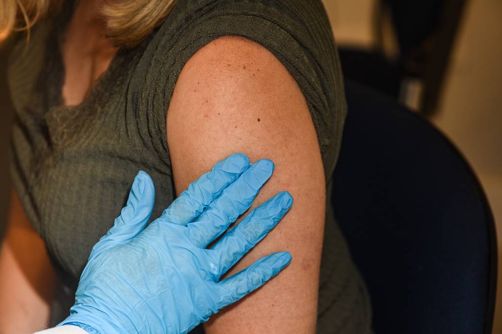 A imagem mostra o braço de uma mulher que acaba de ser vacinada