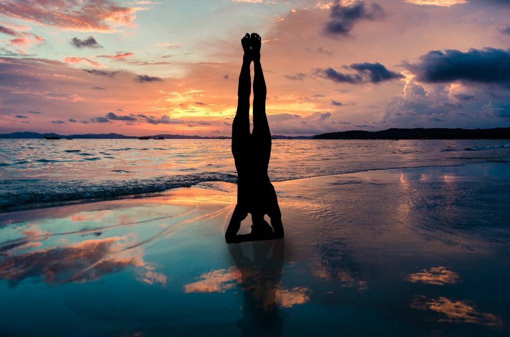 A imagem mostra a sombra de uma pessoa em frente ao mar, de ponta-cabeça, fazendo posição de ioga