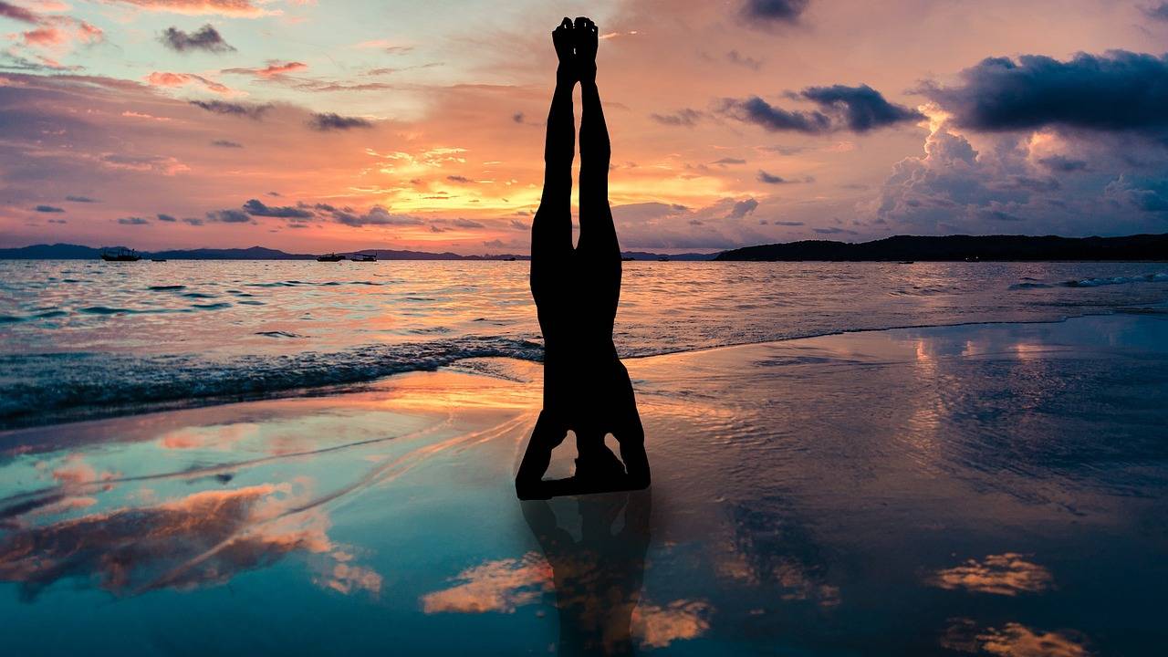 A imagem mostra a sombra de uma pessoa em frente ao mar, de ponta-cabeça, fazendo posição de ioga