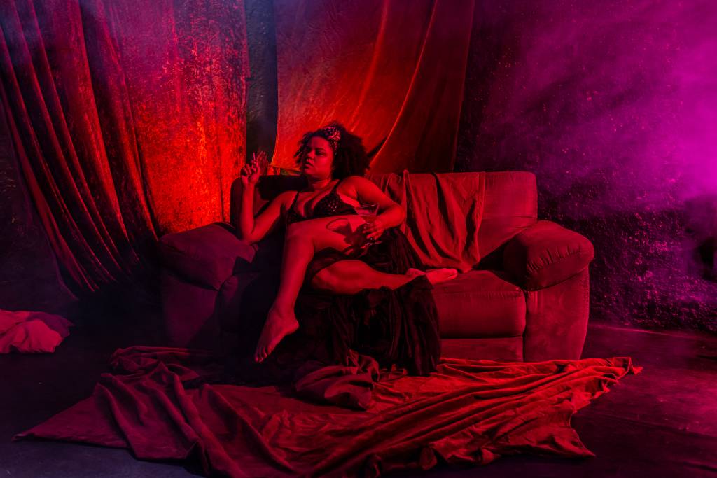 As Mariposas Atriz com roupa íntima sentada num sofá, sob luz vermelha