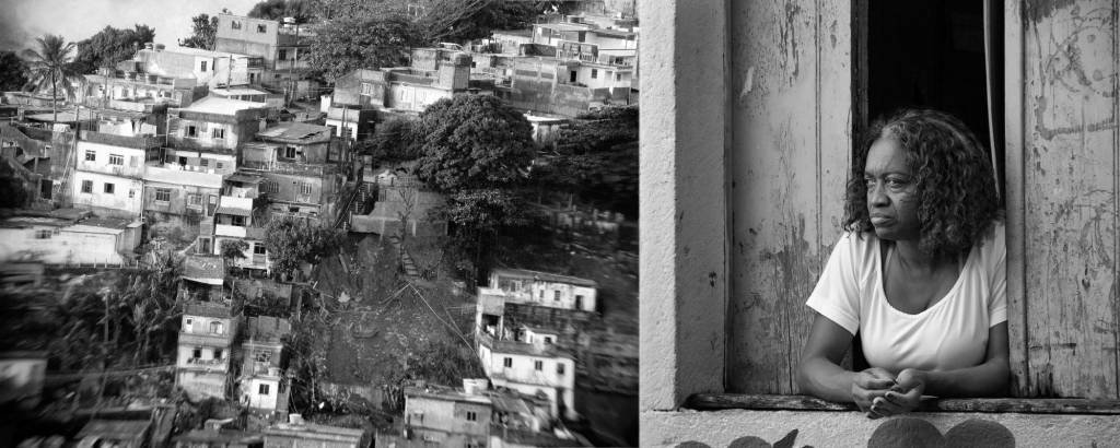 Senhora apoiada na janela de um casa numa favela