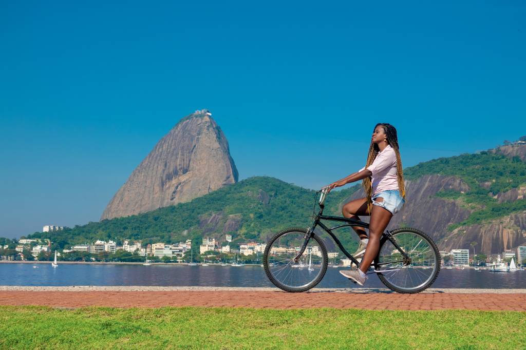 Mulher negra posa com bicicleta com o Pão de Açúcar ao fundo