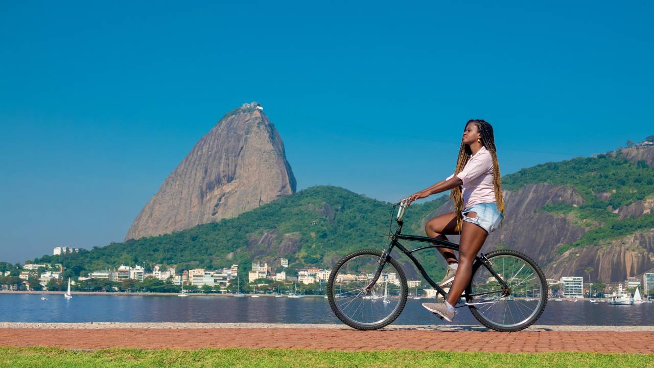 Mulher negra posa com bicicleta com o Pão de Açúcar ao fundo