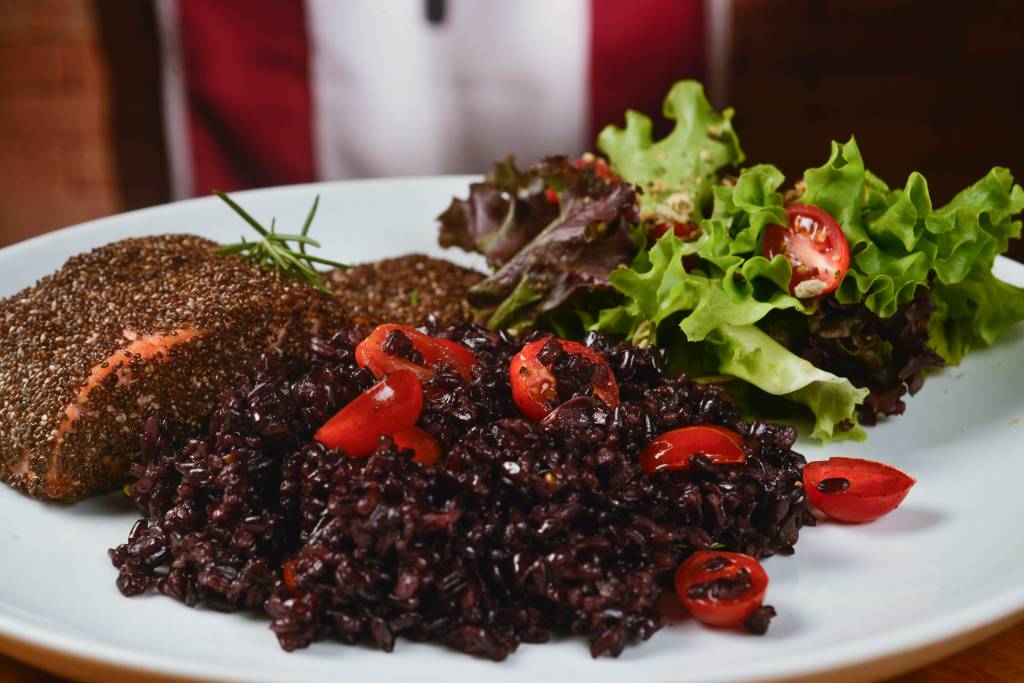 A imagem mostra um prato de salmão em crosta de chia com arroz negro