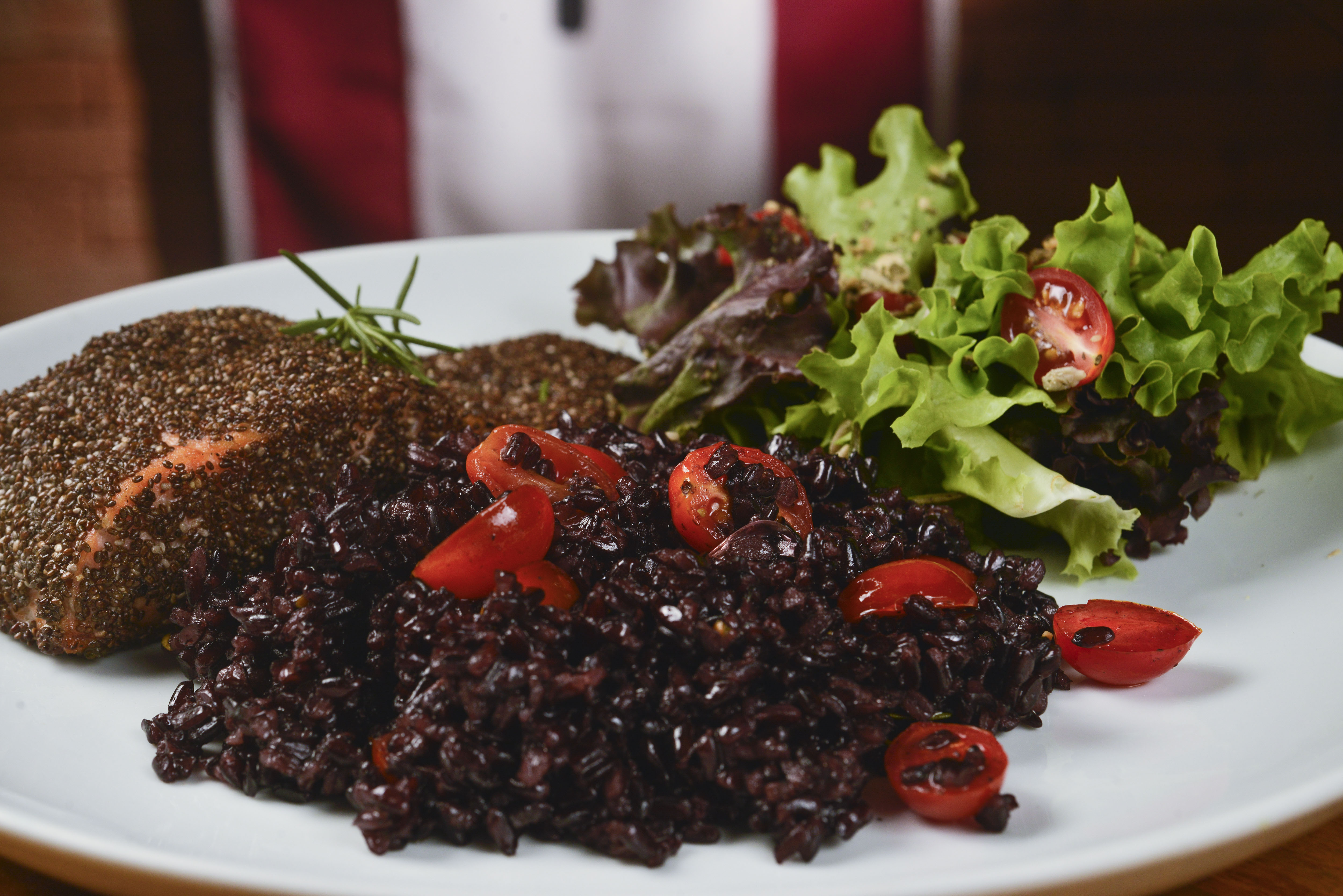O Nórdico – Salmão em crosta de chia A imagem mostra um prato de salmão em crosta de chia com arroz negro