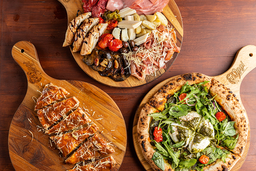 A imagem mostra uma tábua com pizza, frios e pão
