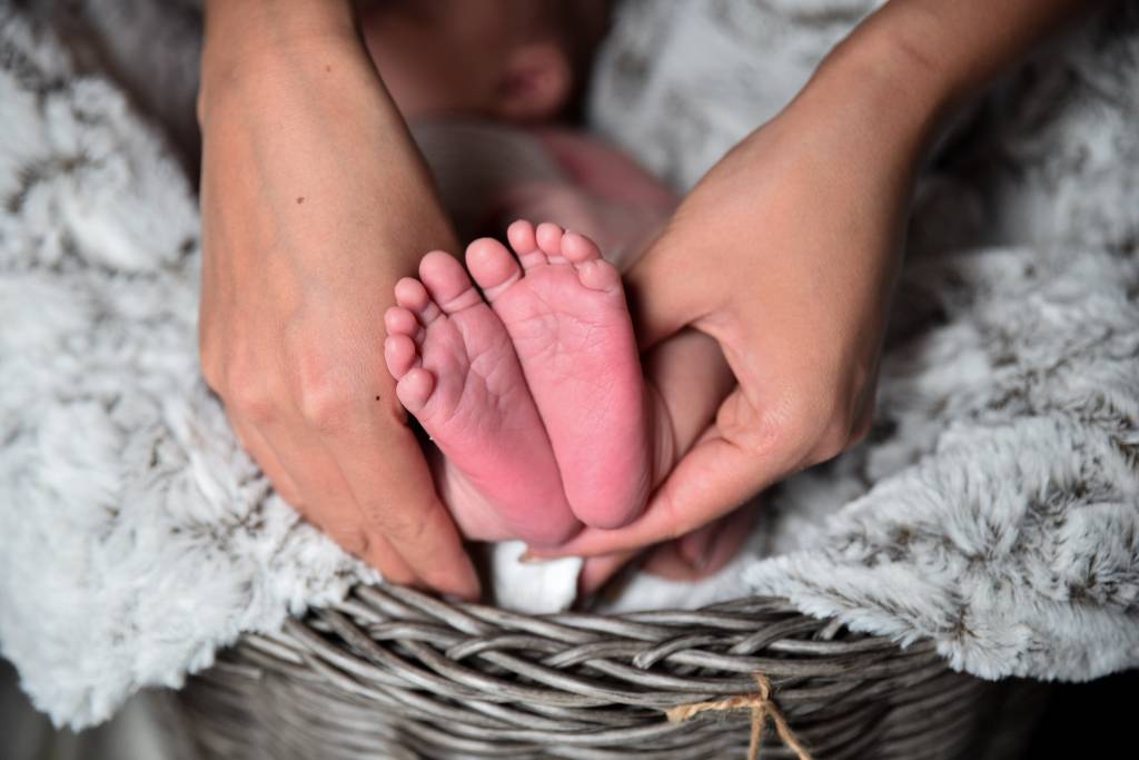 A imagem mostra o pé de um recém-nascido segurado pelas mãos da mãe