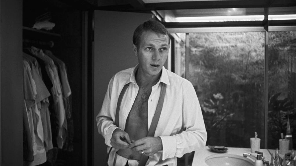 Steve McQueen com camisa de botão aberta num quarto