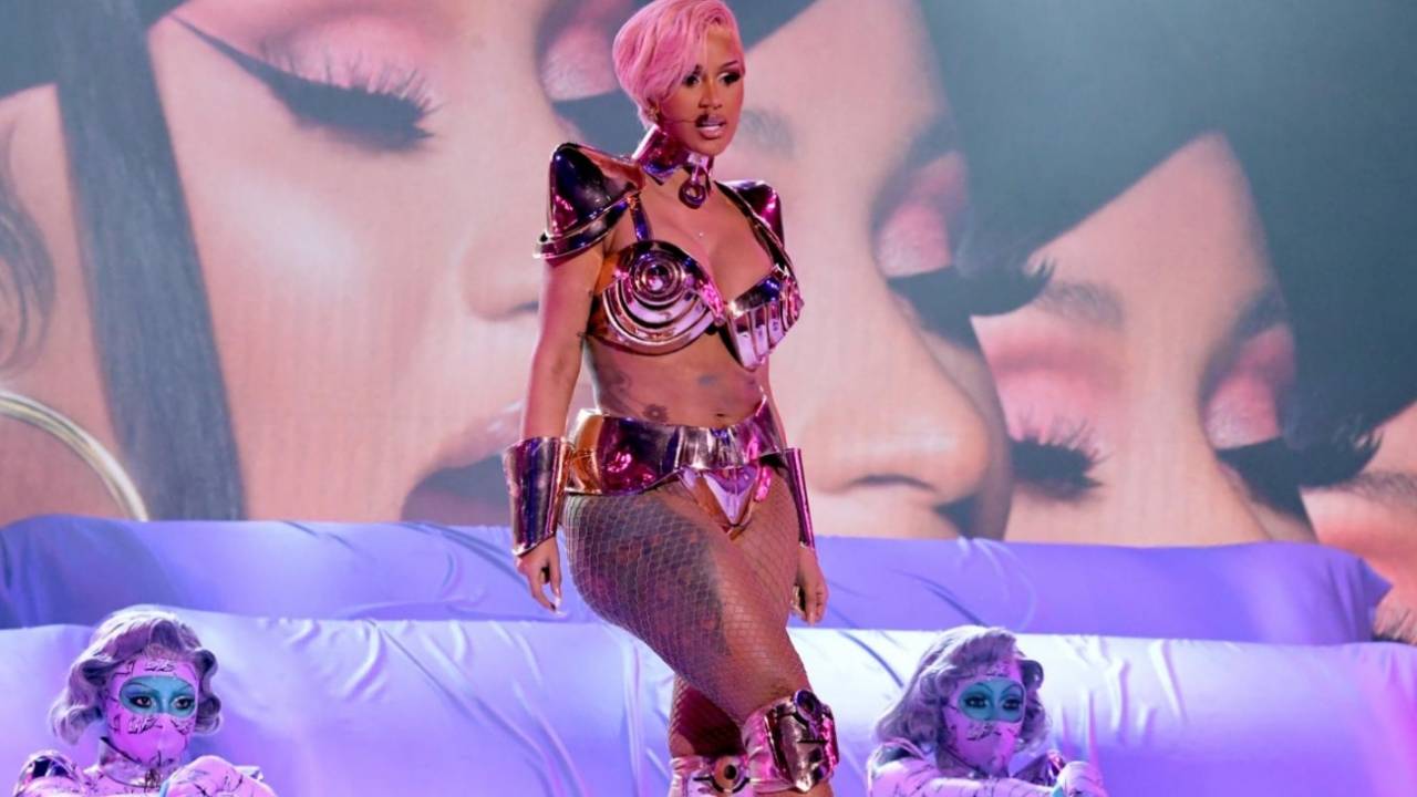 A imagem mostra a cantora Cardi B, de cabelo rosa, no palco do Grammy Awards