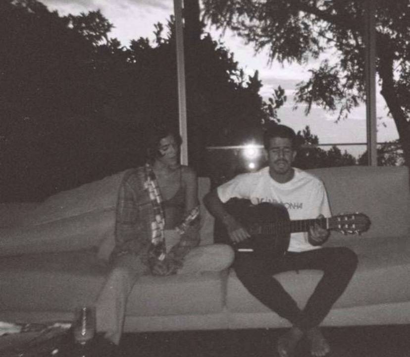 A imagem mostra Enzo Celulari tocando violão, com Bruna Marquezine ao seu lado, num final de tarde
