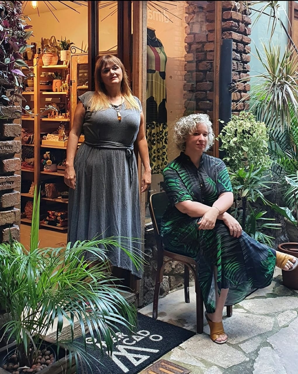 Je e Clarissa Muniz, CASA O Mercado, Vila do Largo_Divulgação Duas mulheres posam na foto, uma sentada com braços cruzados e outra em pé