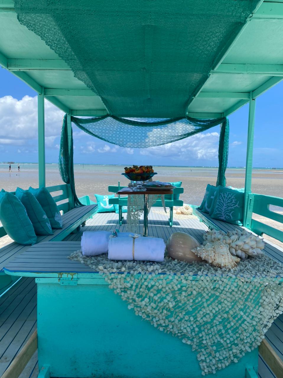 A imagem mostra uma mesa posta à beira-mar, com a cor azul predominando