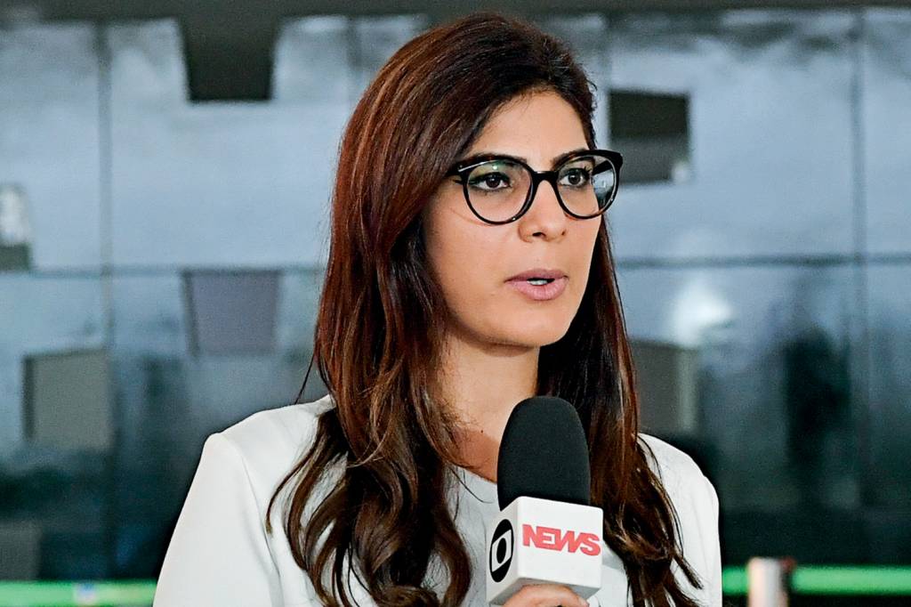 A imagem mostra a jornalista Andreia Sadi, de óculos de grau, segurando o microfone da emissora Globonews