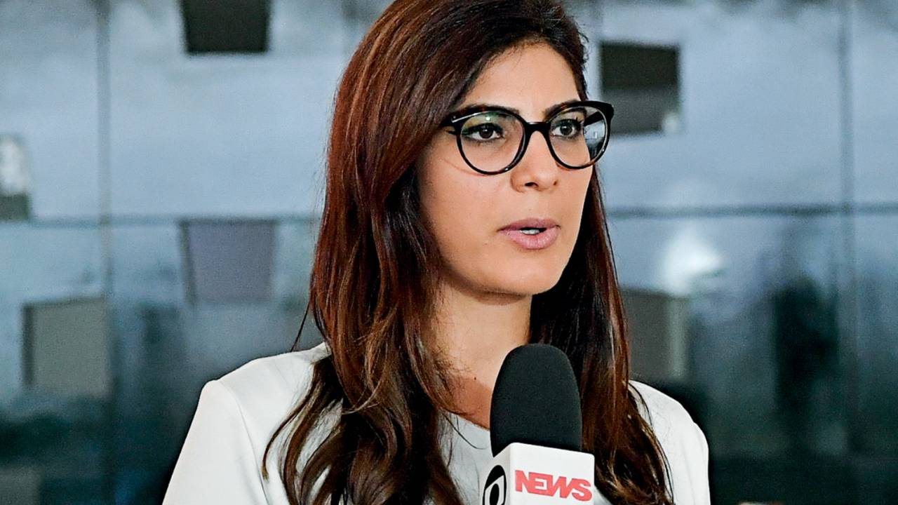 A imagem mostra a jornalista Andreia Sadi, de óculos de grau, segurando o microfone da emissora Globonews
