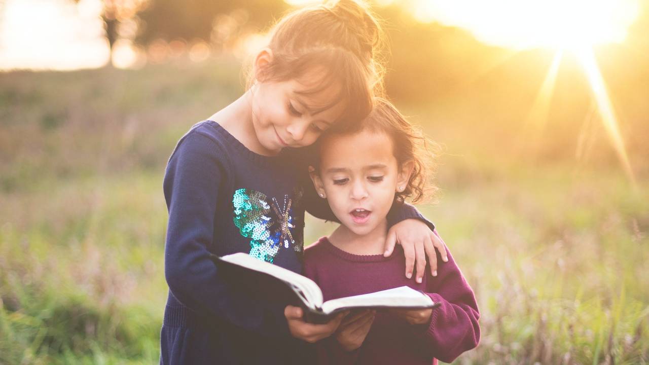 Duas menininhas lendo um livro num campo, ao por do sol