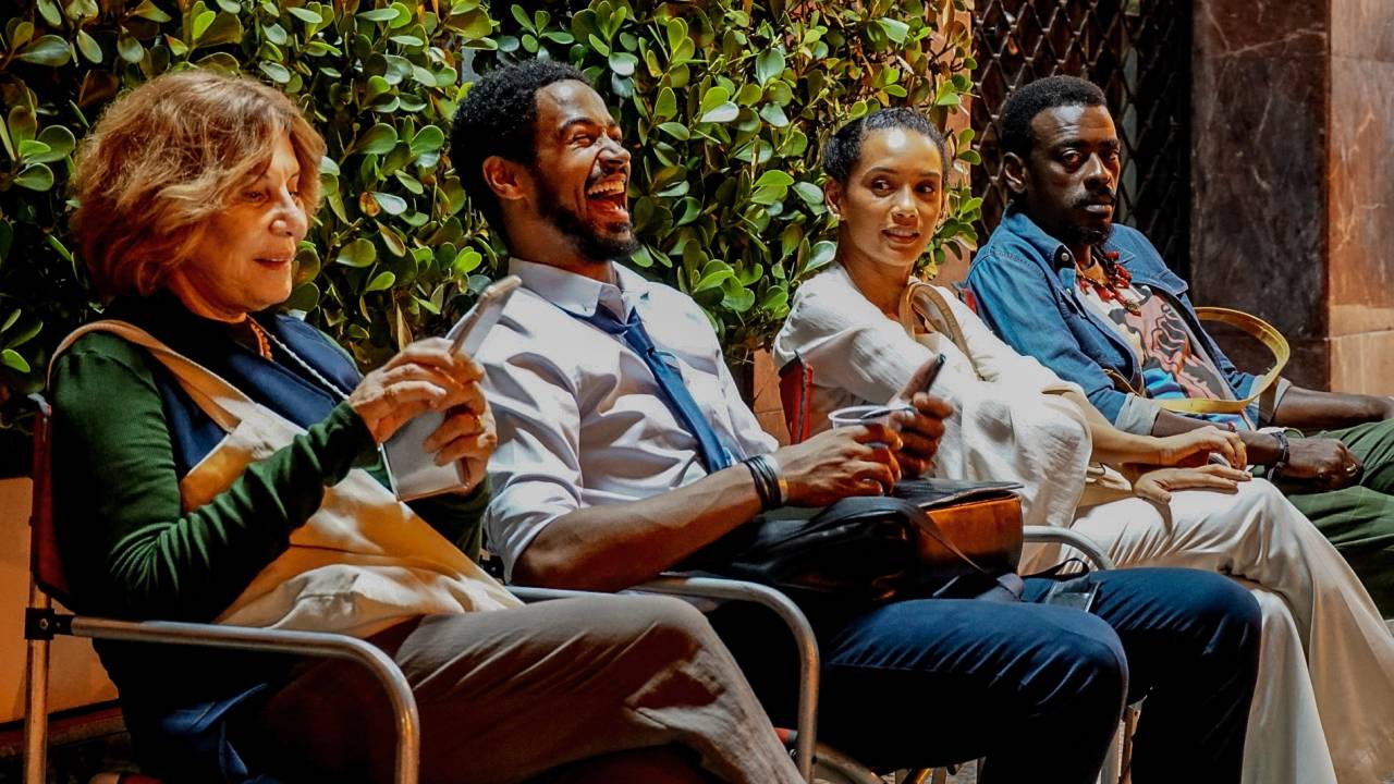 A imagem mostra Renata Sorrah, Alfred Enoch, Taís Araujo e Seu Jorge, sentados em cadeiras, lado a lado