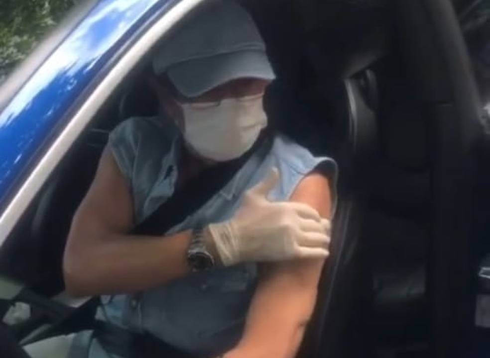 A imagem mostra cantor roberto Carlos dentro de seu carro azul, de óculos de grau, boné e máscara, com a mão no braço que acabara de receber a primeira dose da vacina contra a Covid-19