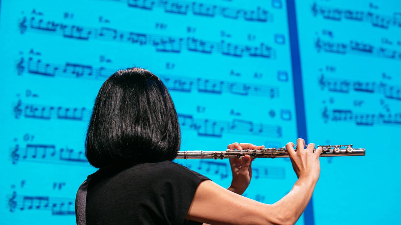 Flautista de costas, tocando o instrumento num palco iluminado de azul