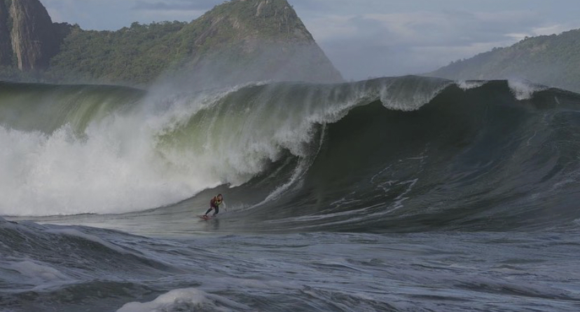 A imagem mostra um surfista pegando uma onda gigante na Baía de Guanabara