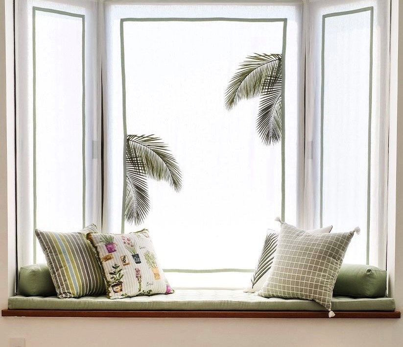 Imagem mostra a bay window com sofá, almofads e e uma cortina estampada.