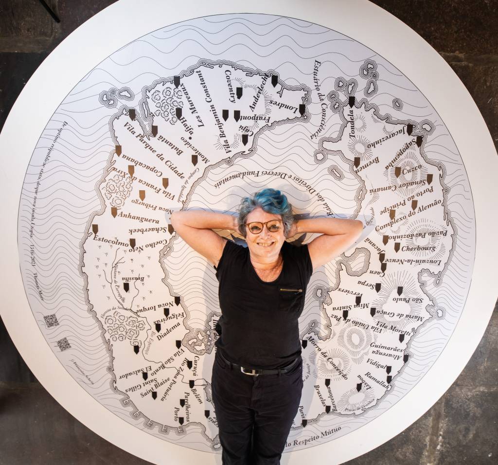 Artista Françoise Schein posa na frente de um de seus painéis, que representa um mapa mundi