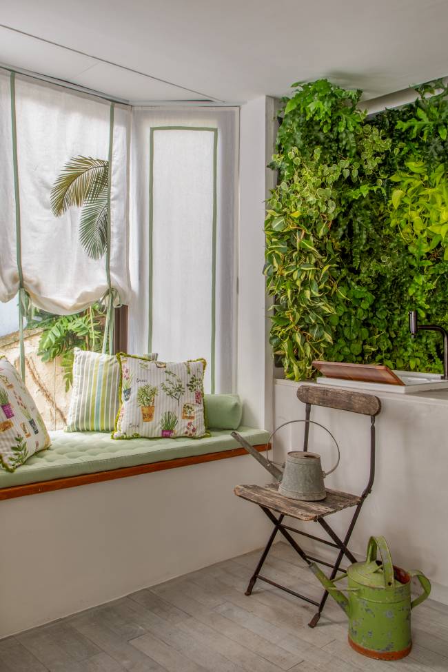 Imagem mostra uma bay window com sofá, almofadas e uma cortina estampada. Ao lado um jardim vertical.