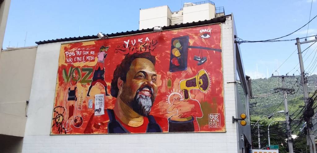 Mural em tons de vermelho com rosto de Marco Yuka e elementos como sinal de transito e menino que vende bala na rua