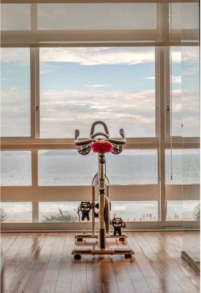 Imagem mostra a bicicleta na sala com vista para o mar.