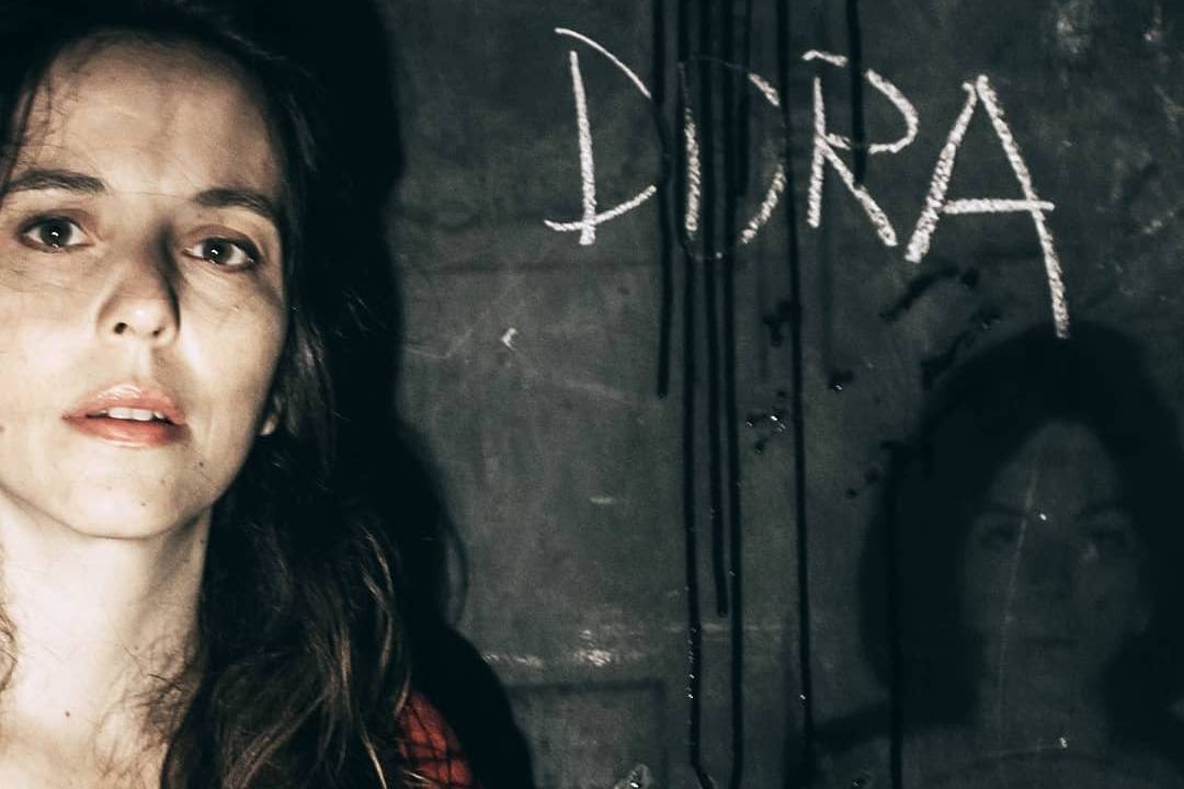 Sara Antunes na frente de uma parede com a palavra Dora escrita em giz