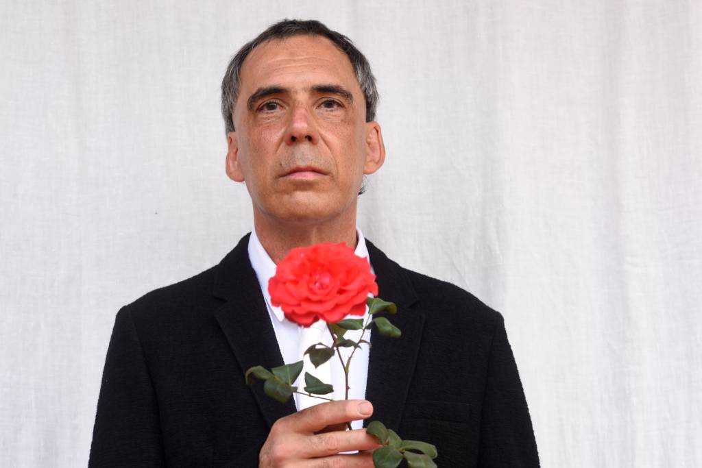 Arnaldo Antunes, de paletó, segurando uma rosa