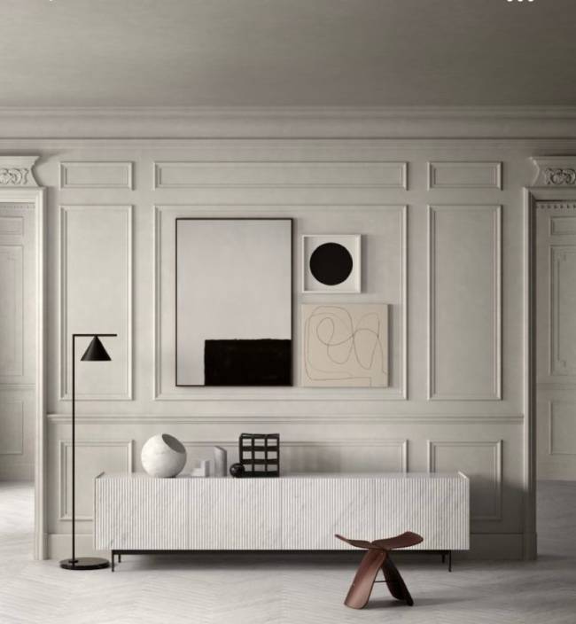 Boiserie A imagem mostra uma parede com boiserie e quadros. Em segundo plano um aparador e uma luminária de piso.