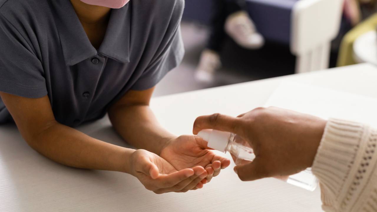 Criança de máscara recebendo alcool em gel pra passar nas mãos