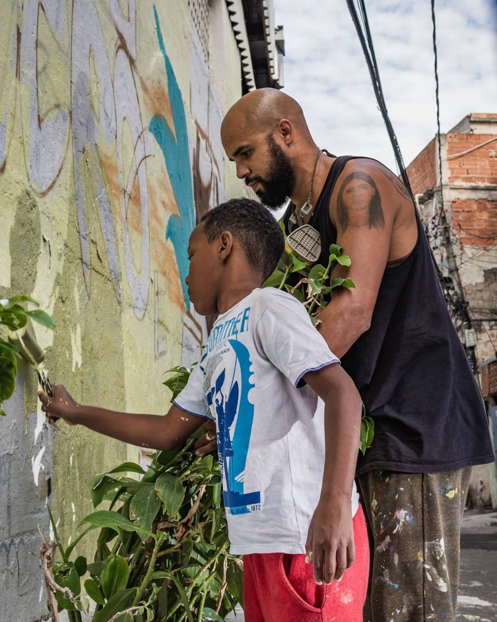 Homem adulto e criança pintam muro