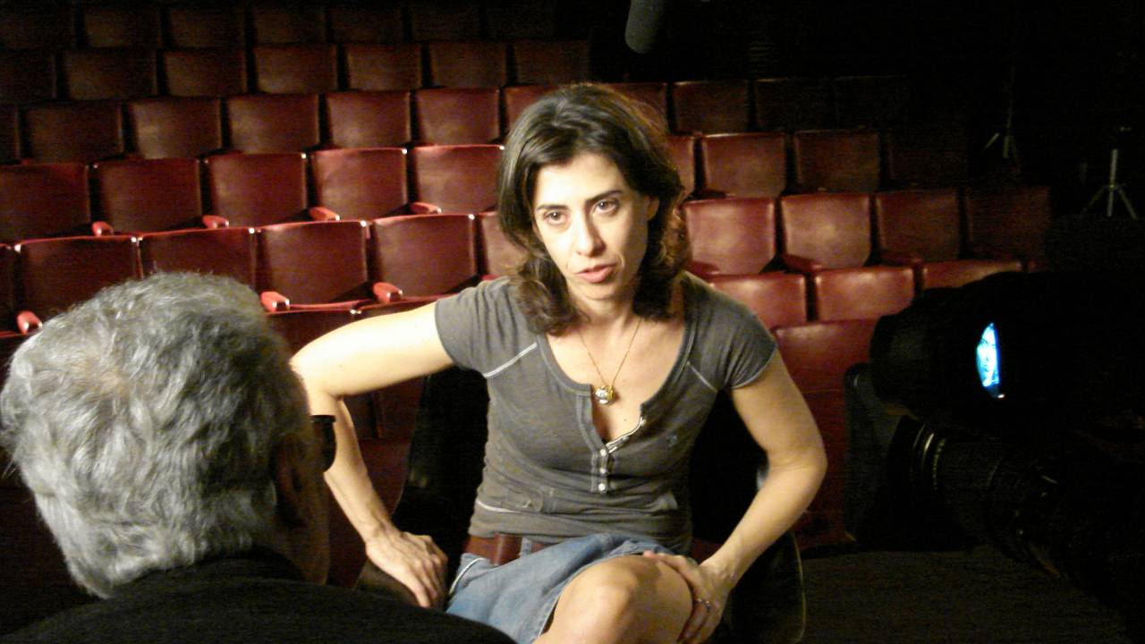 Fernanda Torres, no palco de um teatro, de frente para o cineasta Eduardo Coutinho, que está de costas