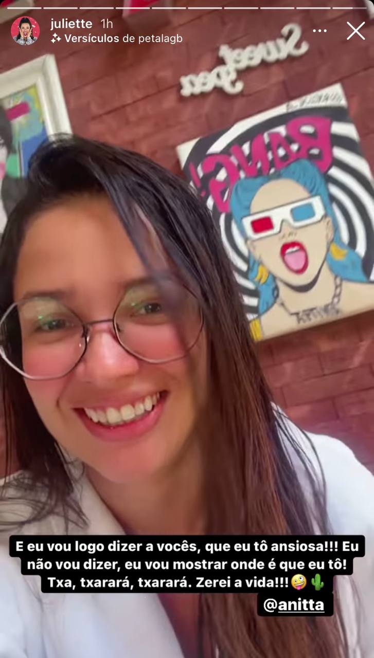 Juliette Juliette, de óculos e cabelos molhados, de roupão, com um quadro de Anitta atrás dela