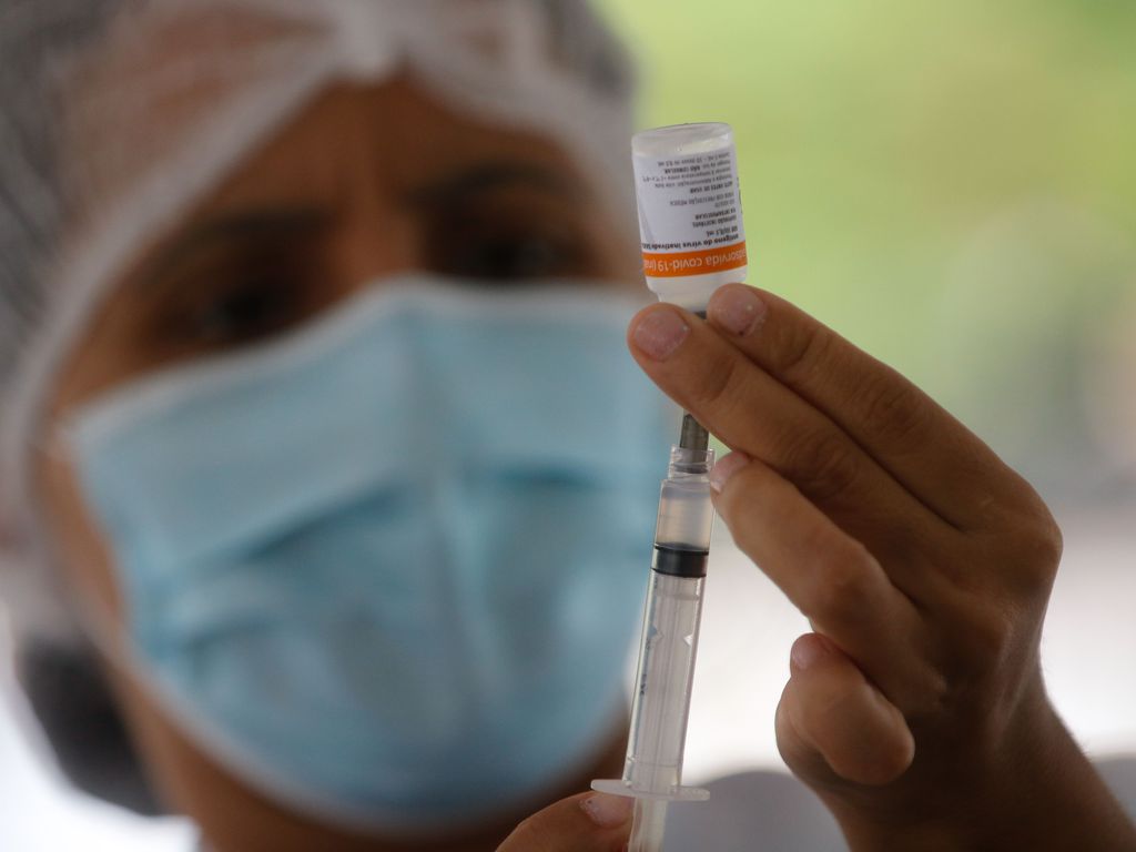 imagem de uma enfermeira com máscara segurando um frasco de vacina