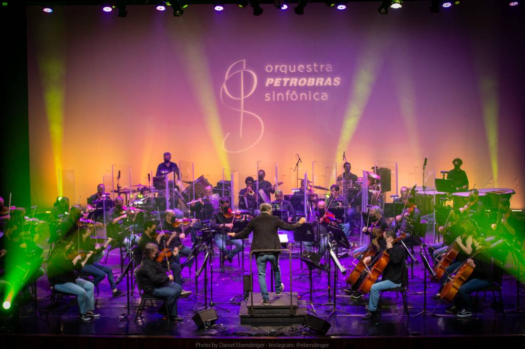 Membros da Orquestra Petrobras Sinfônica no palco, com uma iluminação rosa