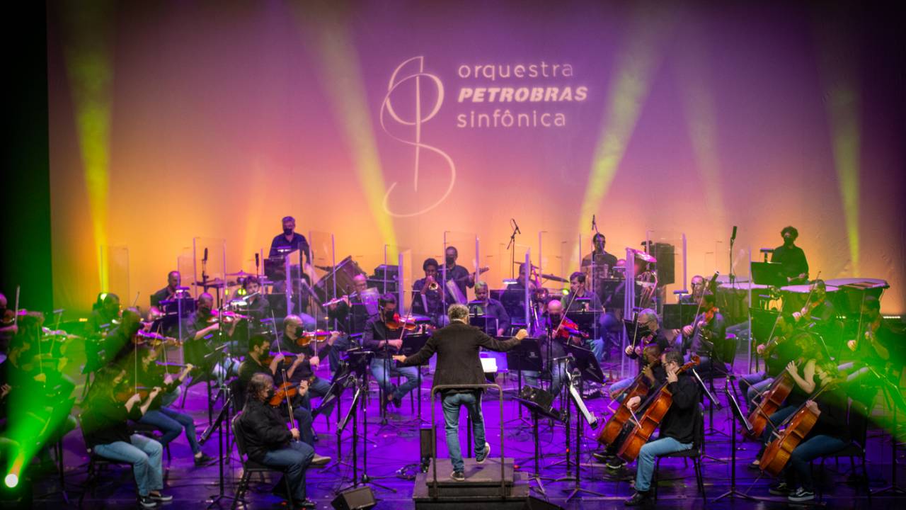 Membros da Orquestra Petrobras Sinfônica no palco, com uma iluminação rosa
