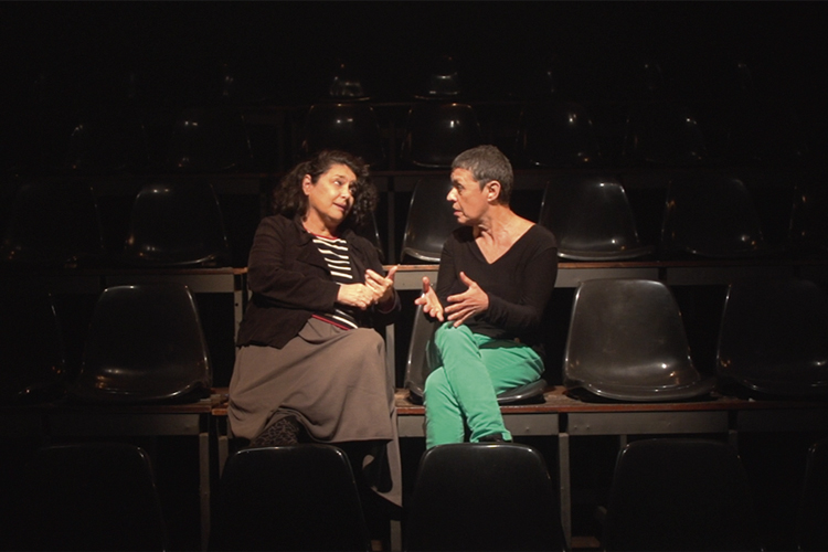 Inez Viana e Denise Stutz sentadas na plateia de um teatro, viradas de lado, conversando