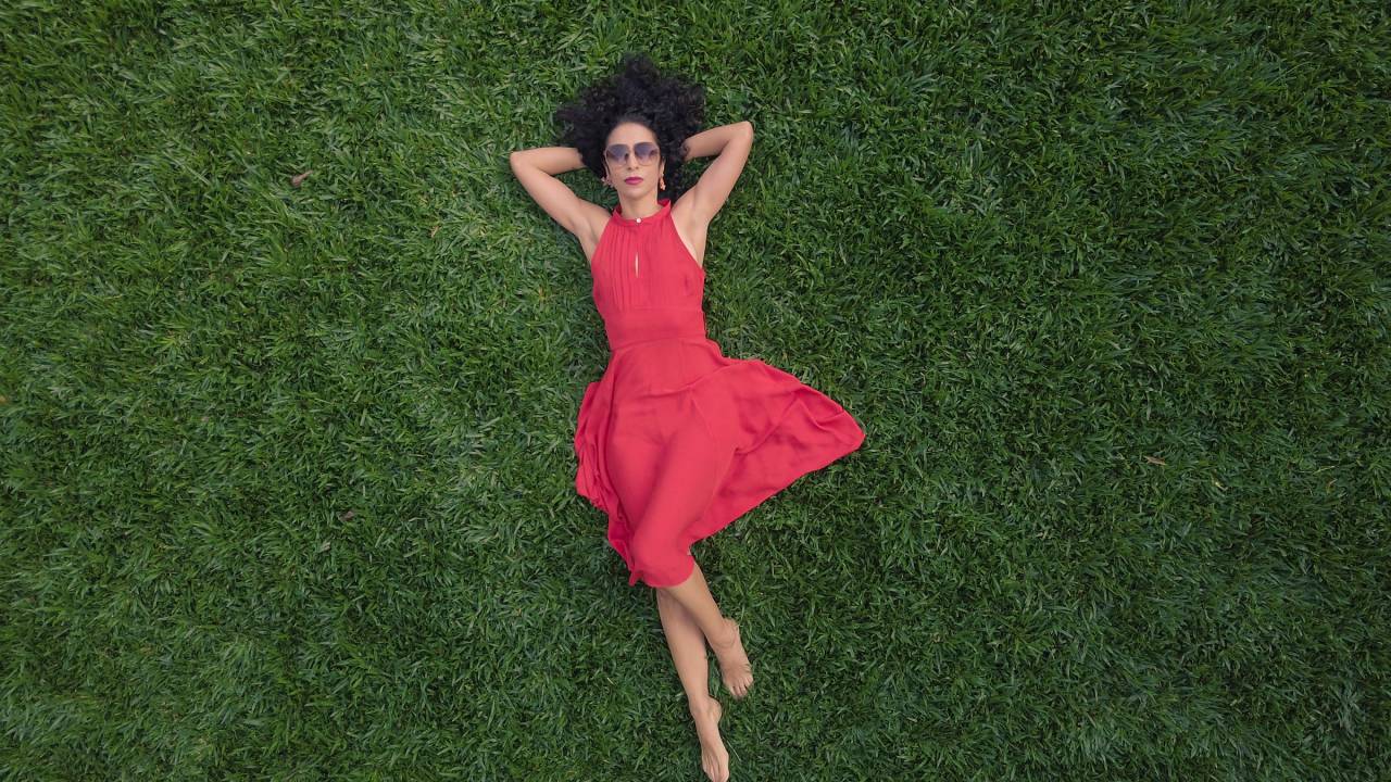Marisa Monte, de vestido cor de rosa, deitada num gramado verde, com as mãos por trás da cabeça