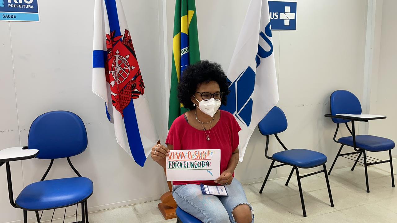 A imagem mostra a cantora Teresa Cristina sendo vacinada e segurando um cartaz onde se lê Fora Genocida e Viva o SUS