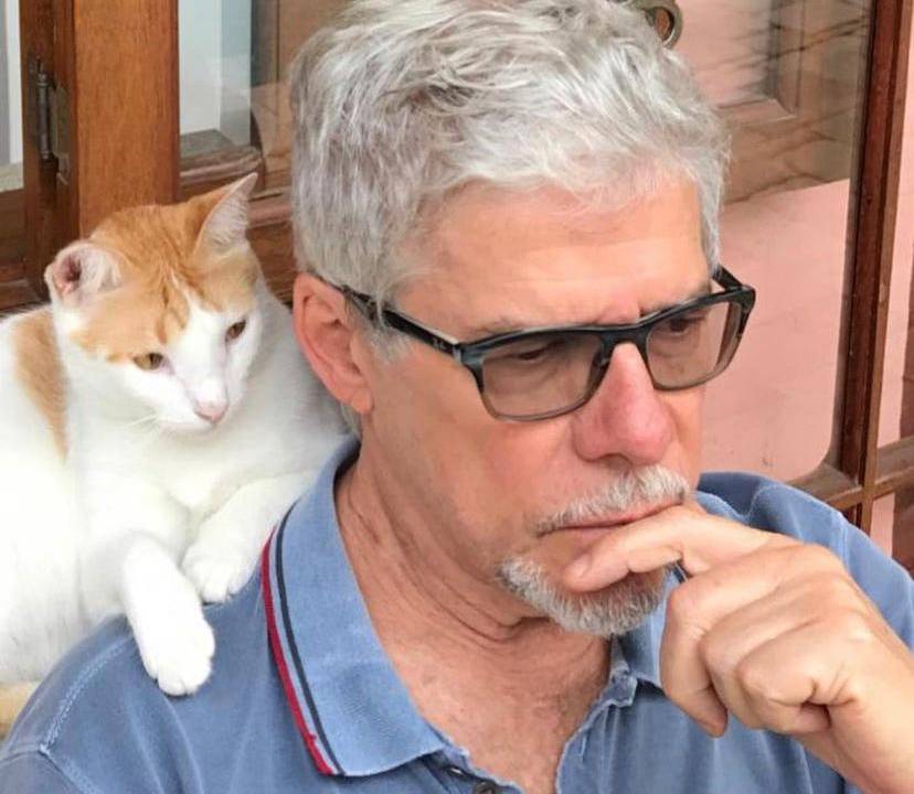 A imagem mostra o ator José Mayer com a mão no queixo e um gato no ombro