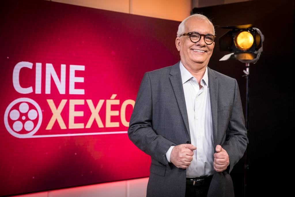 Artur Xexéo em cenário da GloboNews, sorrindo, com as mãos no paletó